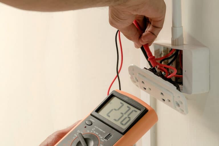 Electrician is using a digital meter to measure the voltage at the power outlet in on the wall.